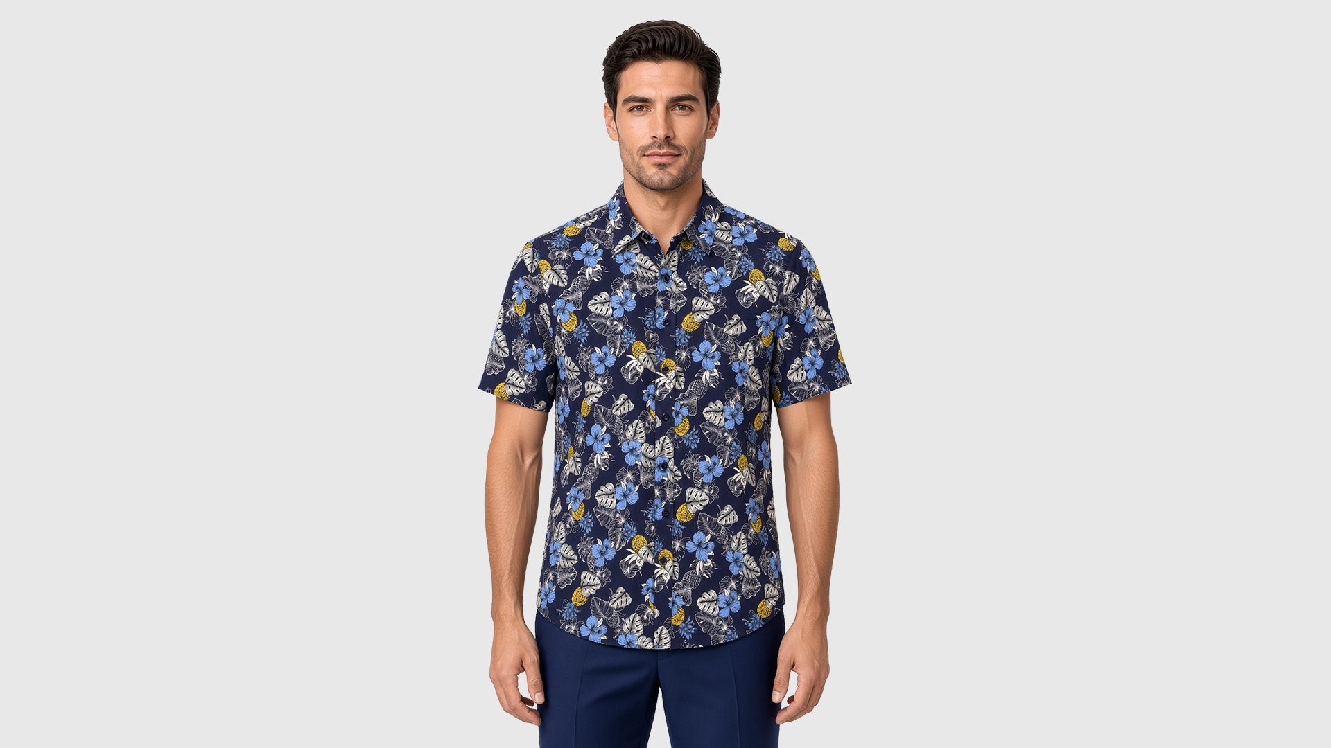 Men’s blue floral short sleeve shirt in cotton, navy ground with powder-blue hibiscus, grey monstera and yellow accents, soft collar, modern fit, worn untucked.